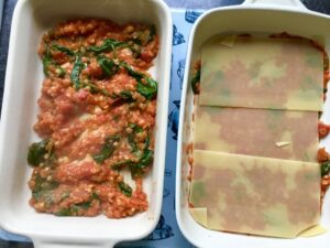 Lasagne assembly with pasta sheets on top of ragu.