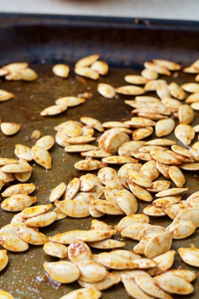 Raw pumpkin seeds covered in seasoning on a baking tray.