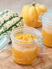 Pumpkin puree in a jar with pumpkins behind it.