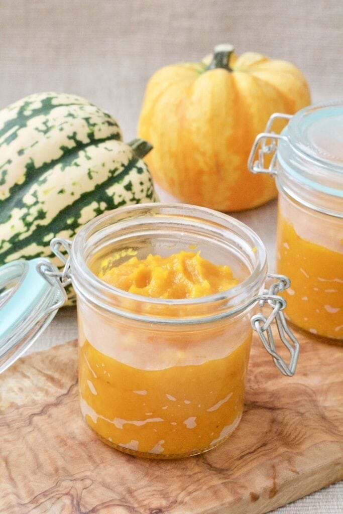 Pumpkin puree in a jar with pumpkins behind it.