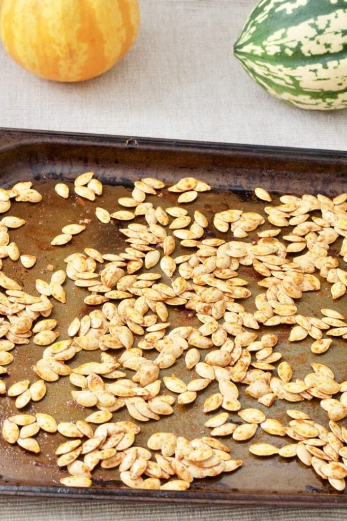 Raw pumpkin seeds covered in seasoning on a baking tray.