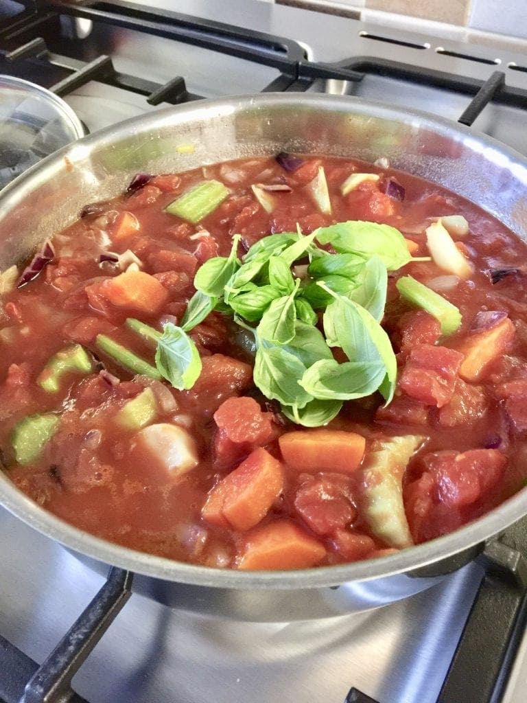 Chopped tomatoes and basil added to vegetables in a pan.