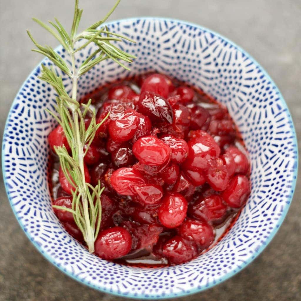 Cranberry sauce in a serving bowl with a sprig of rosemary.
