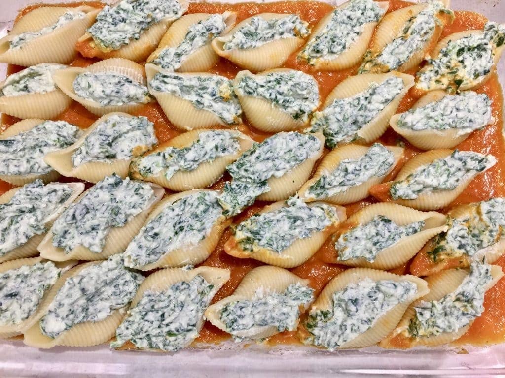 Filling stuffed pasta shells on top of tomato sauce in a dish.