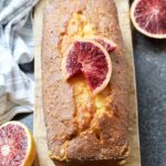 Easy Blood Orange Drizzle Cake on a board decorated with blood orange slices.