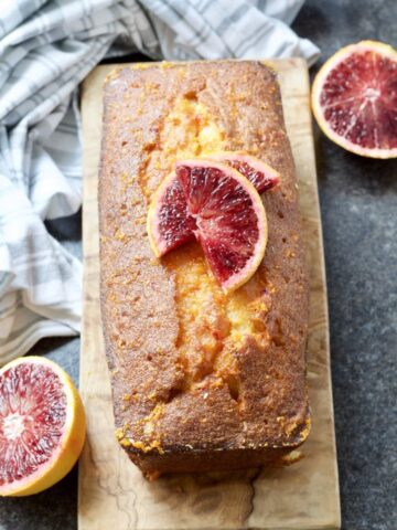 Easy Blood Orange Drizzle Cake on a board decorated with blood orange slices.