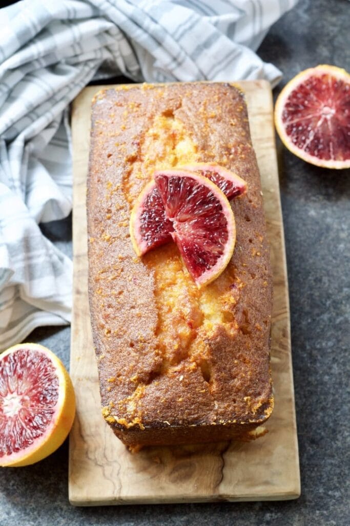 Easy Blood Orange Drizzle Cake on a board decorated with blood orange slices.