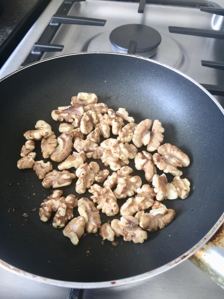 Walnuts toasting in a frying pan.