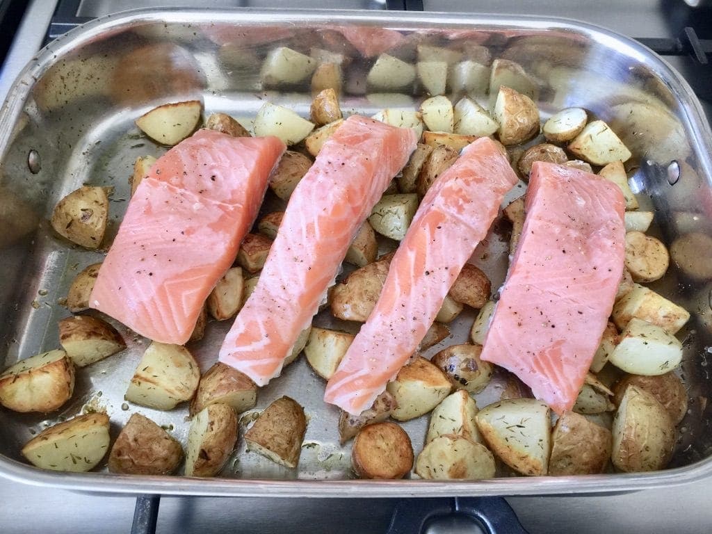 Roasting tray with pre-baked new potatoes and salmon fillets on top.