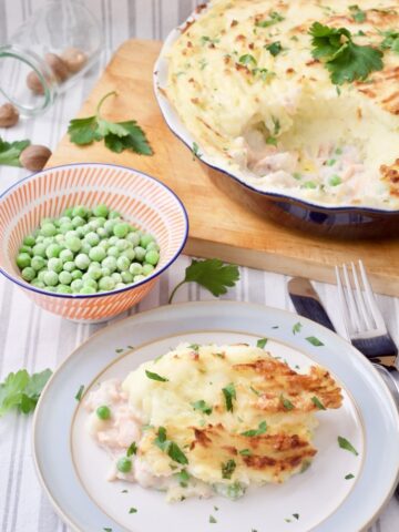 Fish pie in a dish and on a plate with bowl of peas.
