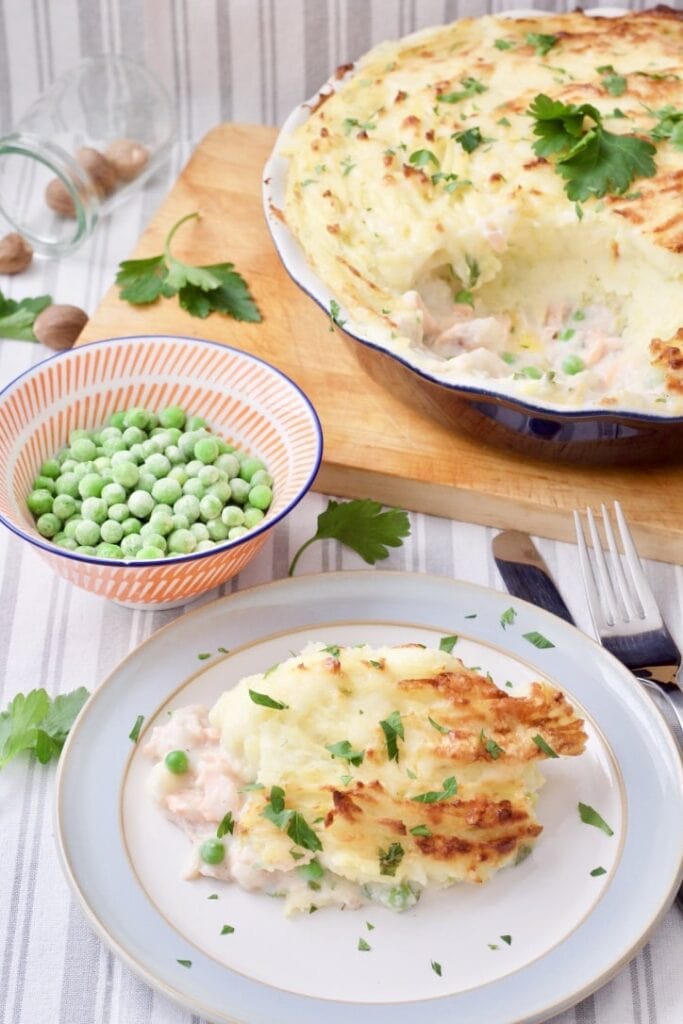 Fish pie in a dish and on a plate with bowl of peas.