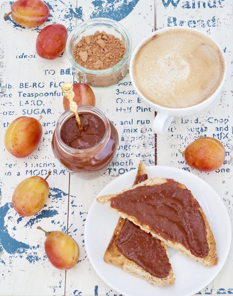 Toast on a plate, plum jam with chocolate, cup of coffee.