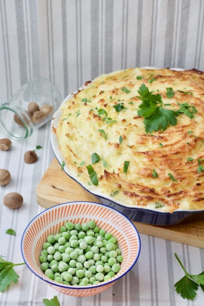 Baked pie sprinkled with parsley and bowl of peas.