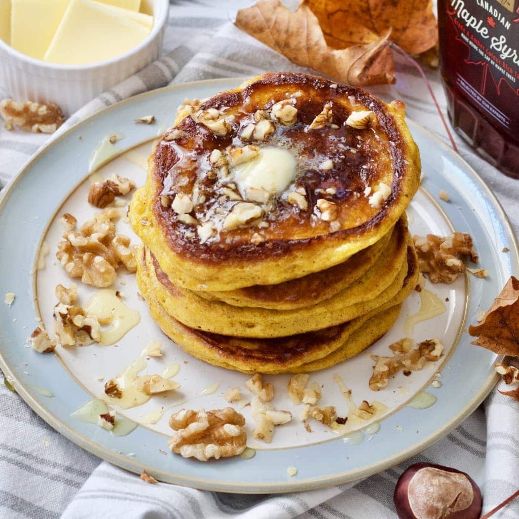 Plate with pancake stack, walnuts and melting butter on top.