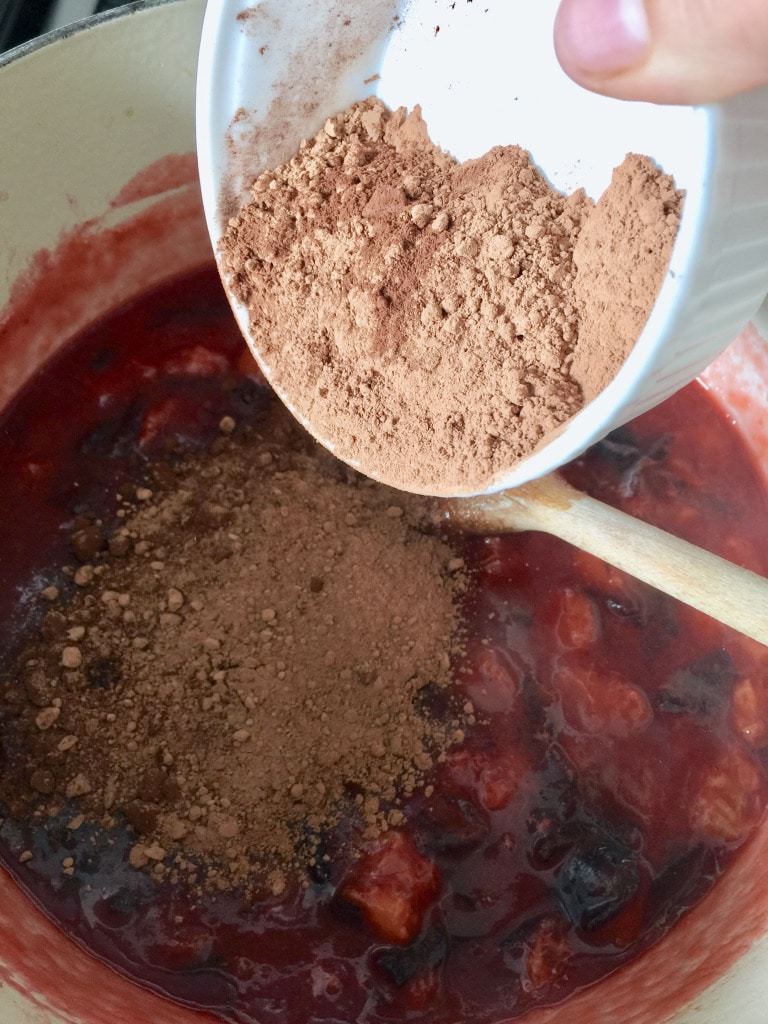 Cocoa powder in a bowl over a pot with plums.