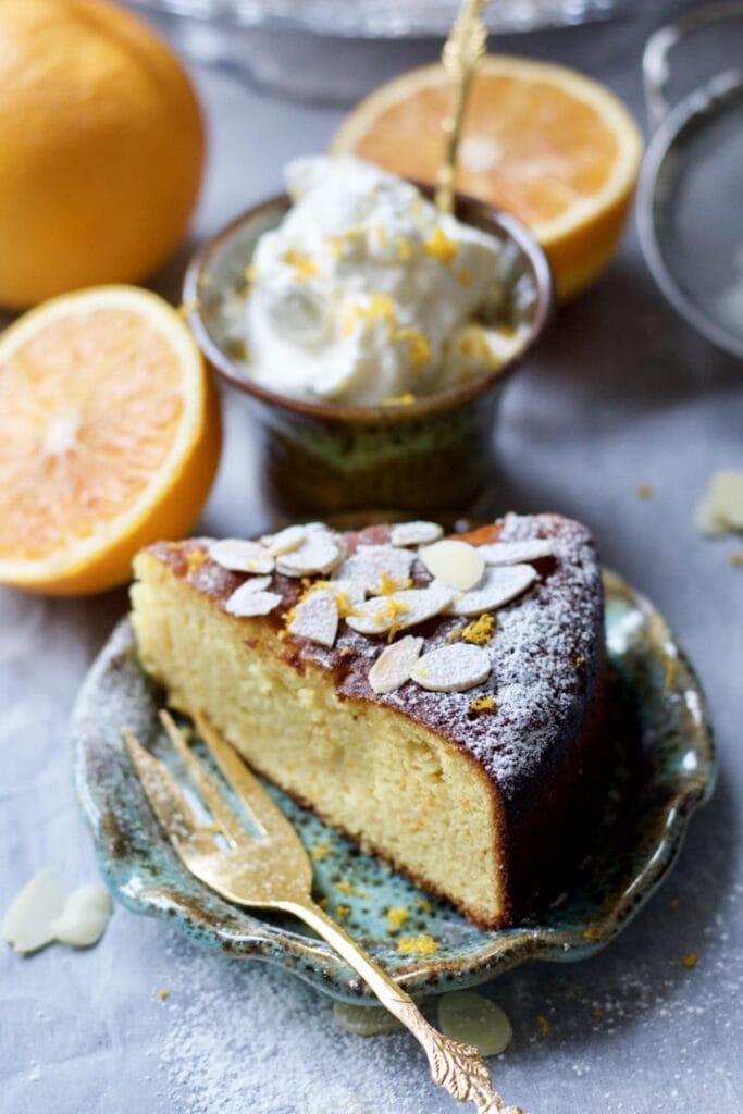 Slice of Gluten-Free Orange and Almond Cake with orange whipped cream and orange halves in the background