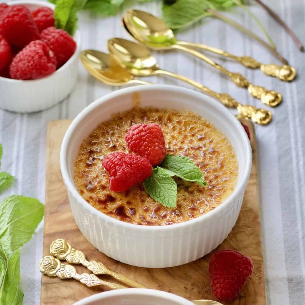 Creme Brulee with mint and raspberries on a wooden board (close-up).