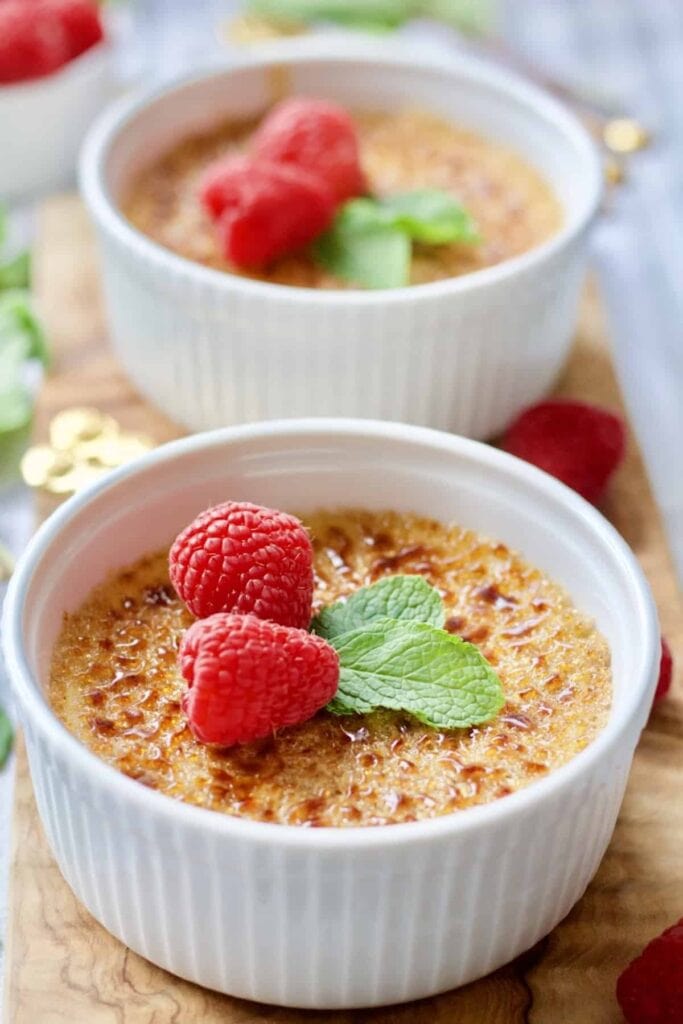 Creme Brulee with mint and raspberries on a wooden board.