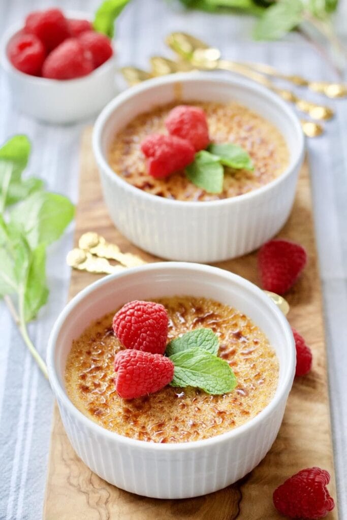 2 creme brûlées in ramekins decorated with mint and fresh raspberries.