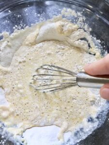 Mixing flour and egg mixture with a whisk to make batter for perfect pancakes.