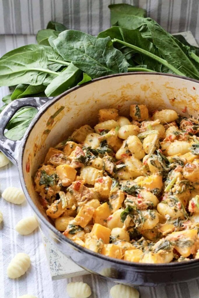 Easy Butternut Squash & Chorizo Gnocchi - close up of pan with ready made dish with some fresh spinach and uncooked gnocchi around it