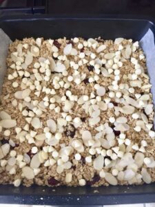 Flapjacks in a baking tin with scattered almonds & white chocolate chips