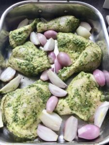 Chicken pieces covered in pesto in baking tray with shallots