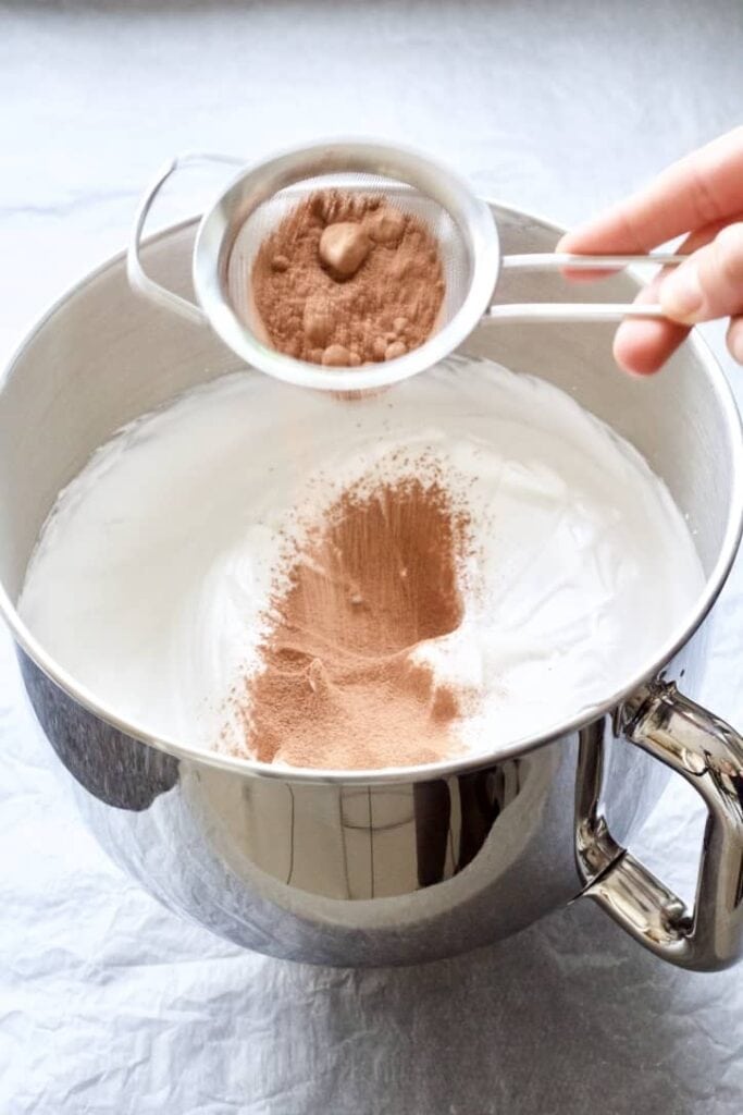 Cocoa powder being sieved into the beaten egg whites.