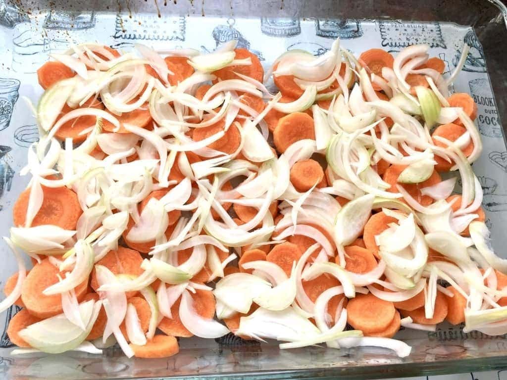 Sliced carrots and onions in a baking dish.