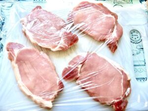 Pork chops on cutting board covered with cling film.