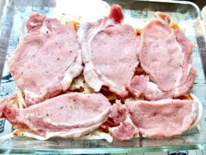 Pork chops on top of veggies in a baking dish.