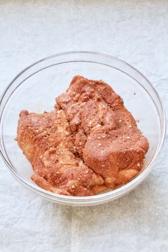 Pork shoulder covered in dry rub in a bowl.
