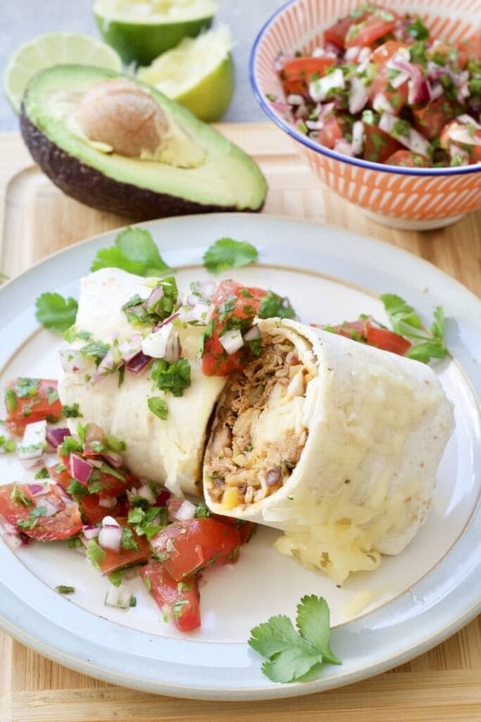 Burrito cut in half on a plate with salsa.