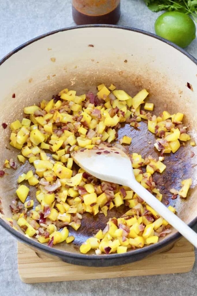 Chopped yellow pepper and red onion in a pan.