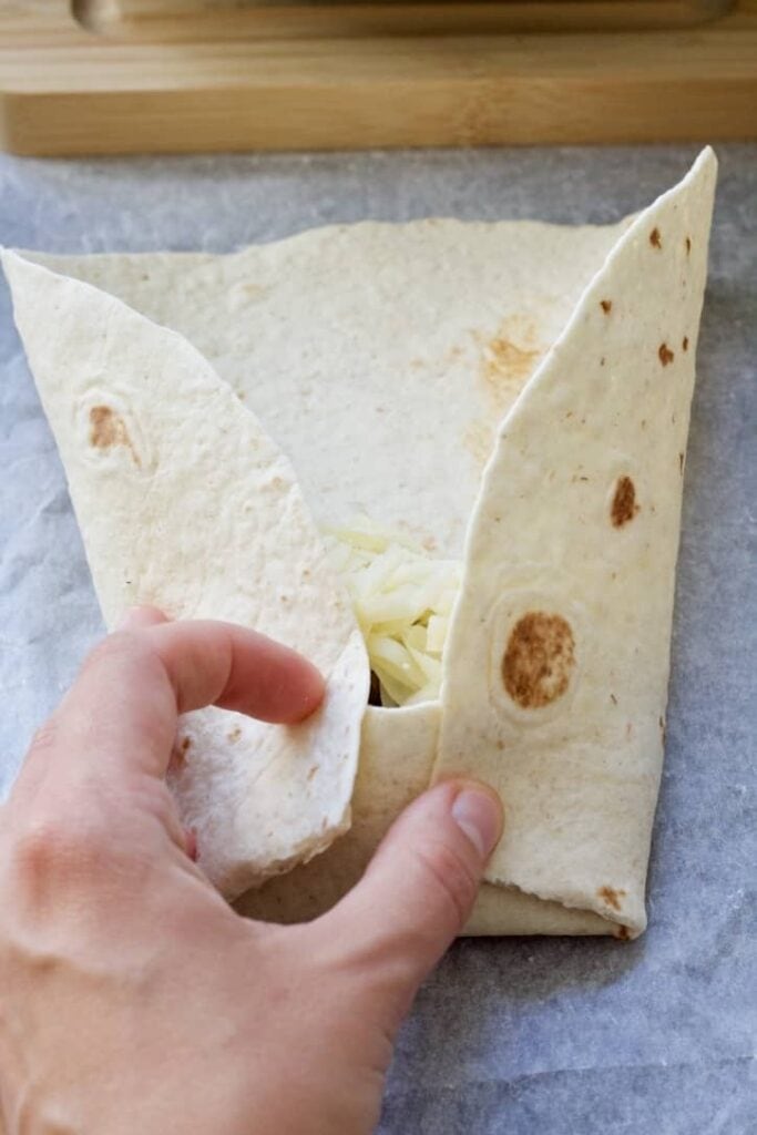 Hand gathering sides of a burrito.