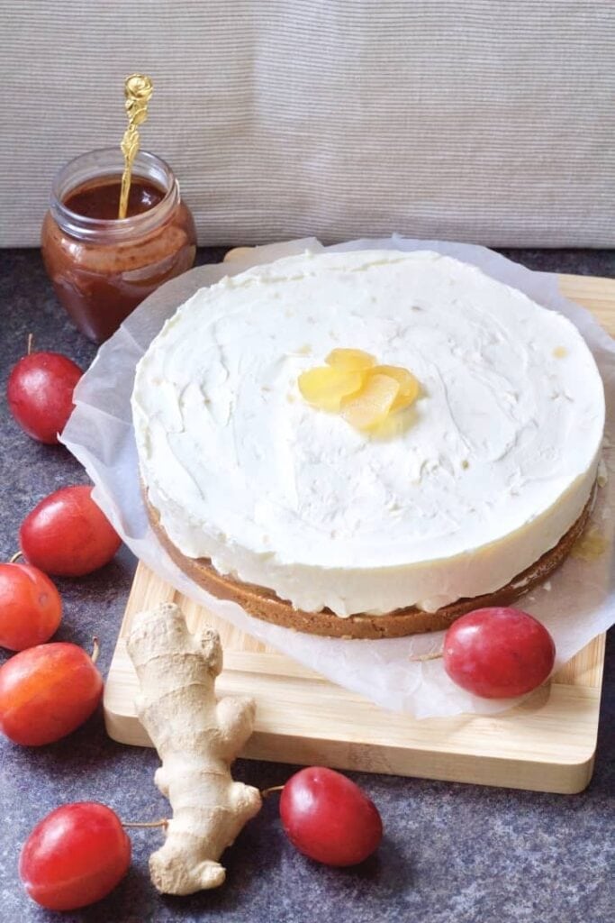 Stem ginger cheesecake on a board with plums & fresh ginger.