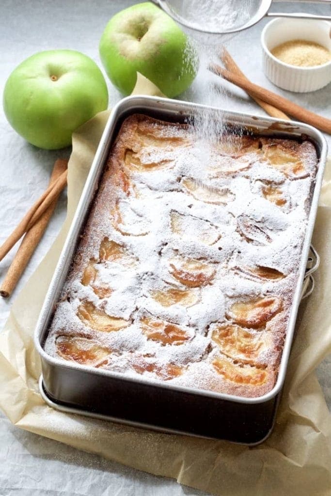 Dorset apple cake sprinkled with icing sugar in a tin.