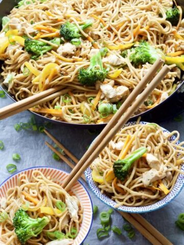 Chicken chow mein in a pan and portions in bowls.