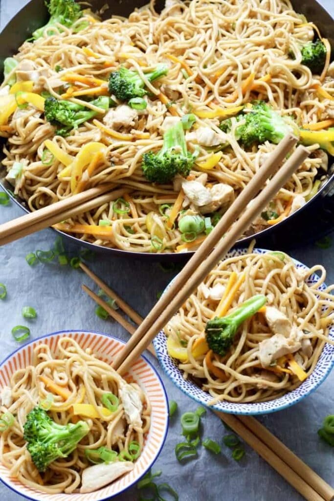 Chicken chow mein in a pan and portions in bowls.