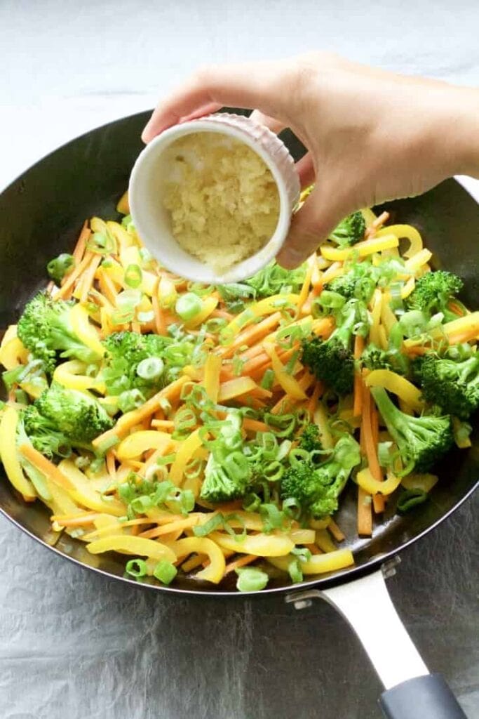 Ginger & garlic being added to the veggies in a pan.