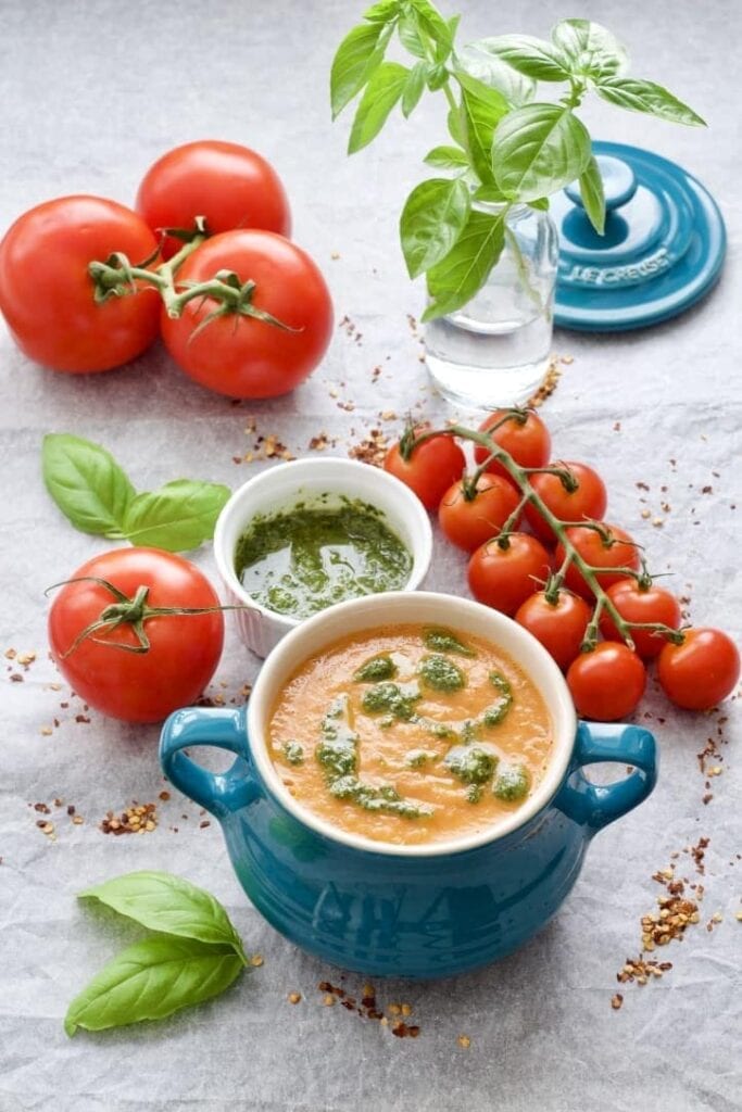 Bowl of tomato & fennel soup with pesto, tomatoes & basil around it.