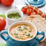 Bowl of tomato & fennel soup with pesto, sliced bread and tomatoes.