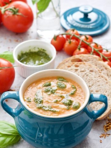 Bowl of tomato & fennel soup with pesto, sliced bread and tomatoes.