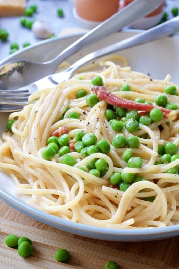 Spaghetti in a bowl with peas, bacon & black pepper on top.