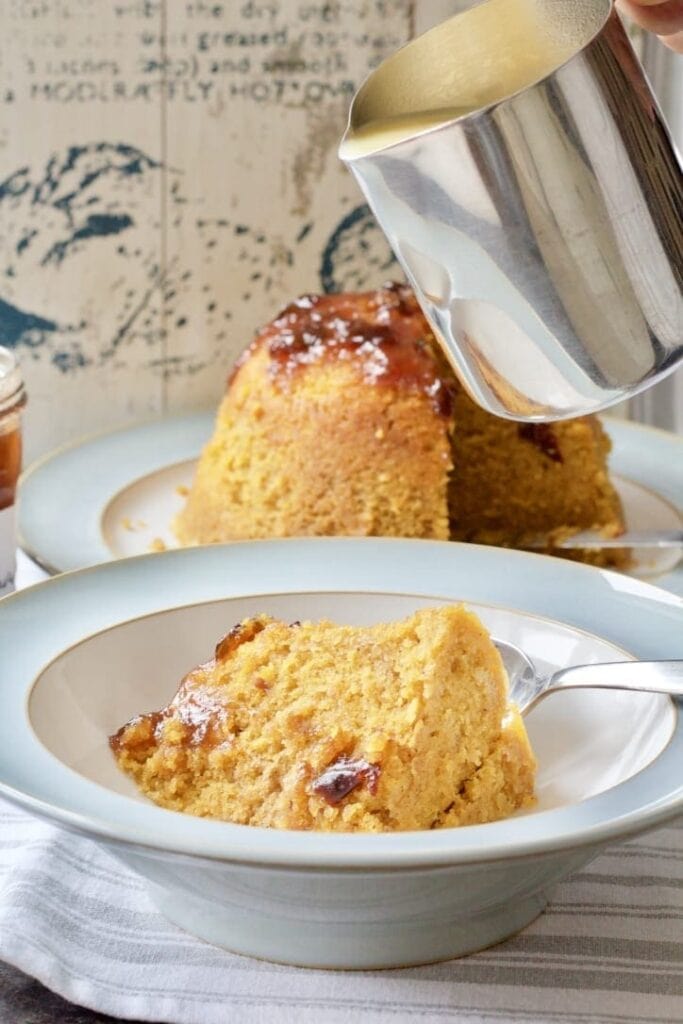 Bowl with slice of steamed pudding and jug with custard over it.