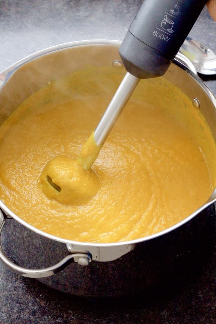 Pumpkin soup being pureed with a stick blender.