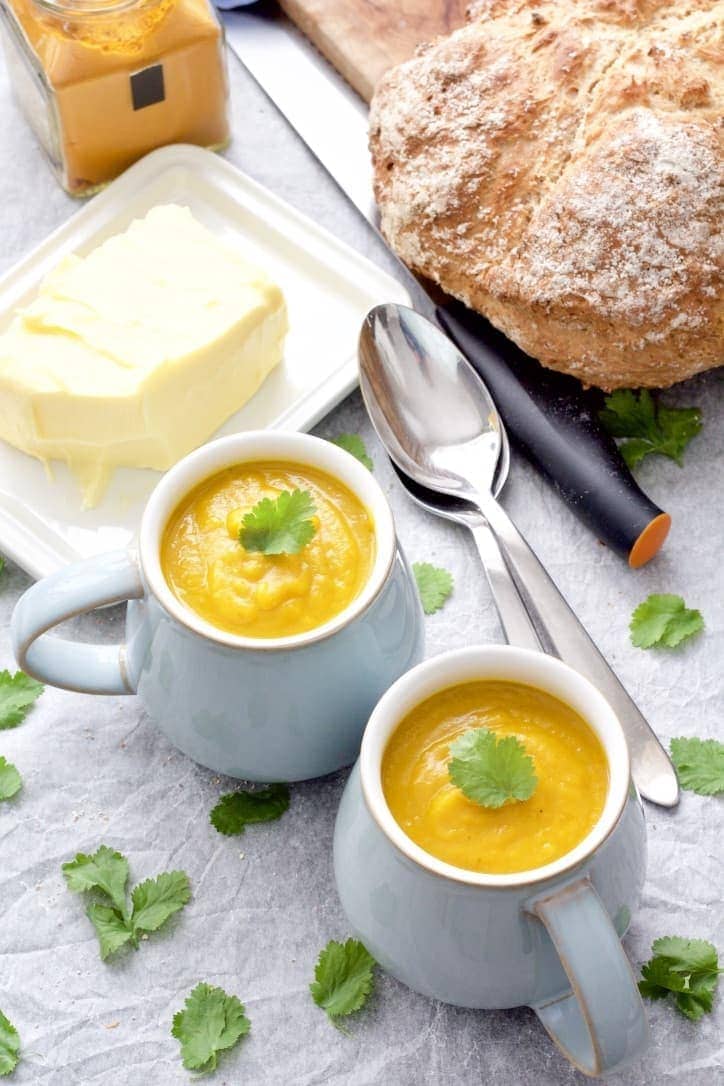 Two mugs of soup, butter in a dish and soda bread.