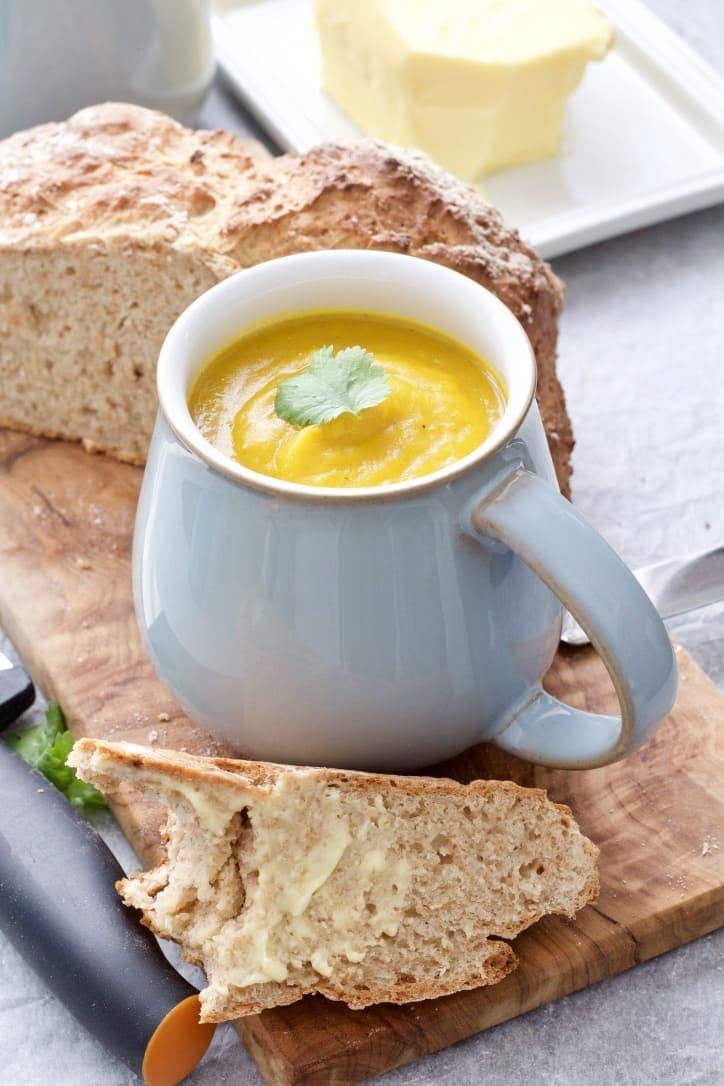 Soup in a mug on a board with slice of bread.