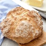 Soda bread loaf on a board with bread knife and butter.