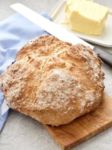 Soda bread loaf on a board with bread knife and butter.